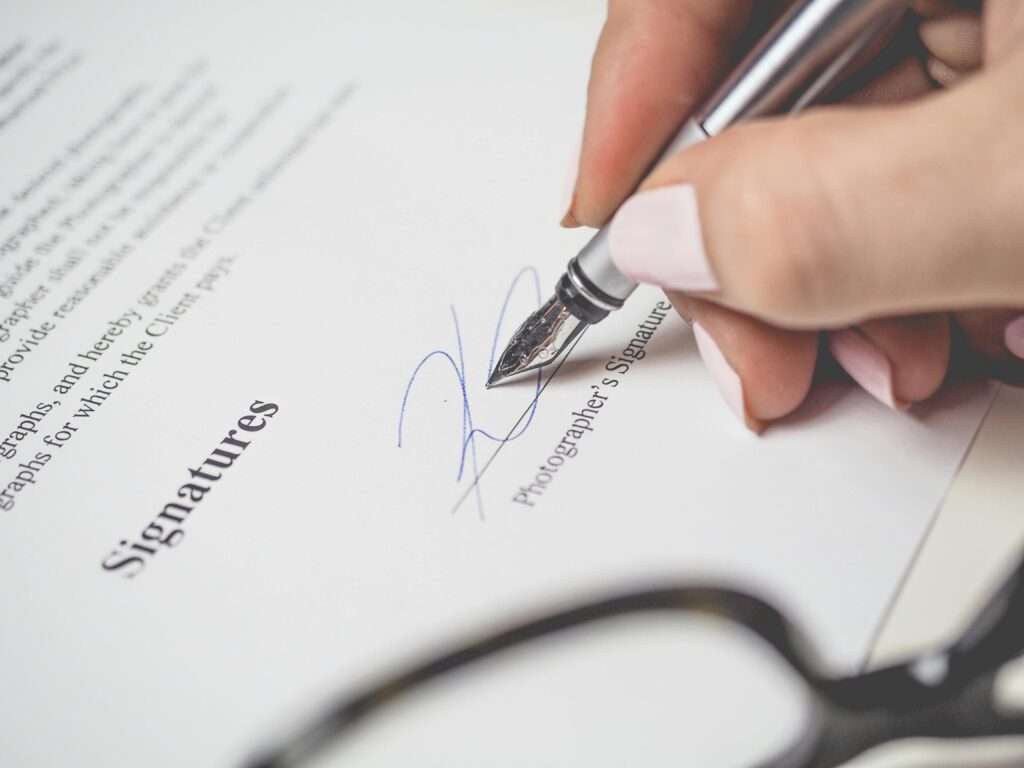 Close-up of a hand signing a contract, showcasing a pen and elegant handwriting.